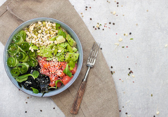 Salted salmon poke bowl with avocado, sea cale, cucumber, sesame seeds and bean sprouts on grey background