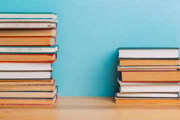 A simple composition of many hardback books, raw books on a wooden table and a bright blue background. Going back to school. Copy space. Education.