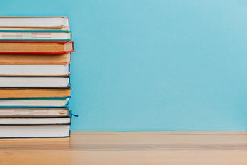 A simple composition of many hardback books, raw books on a wooden table and a bright blue background. Going back to school. Copy space. Education.