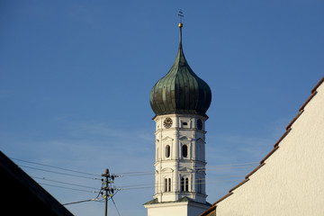 rural onion dome of a church with church clock and in the foreground power cables in bavaria, rural scene with church steeple in bavarian alps