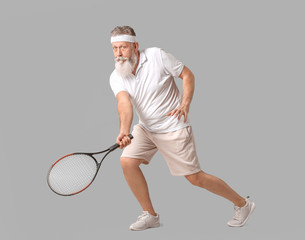 Sporty elderly tennis player on grey background