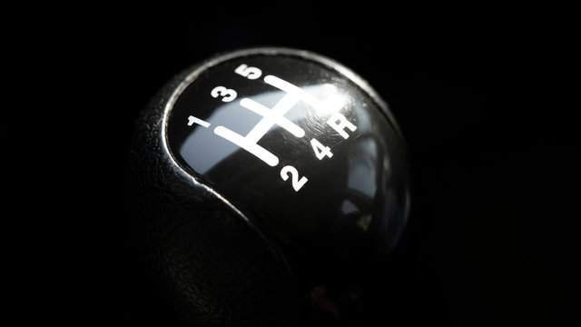 Five-speed gearbox knob on black background, selective focus.