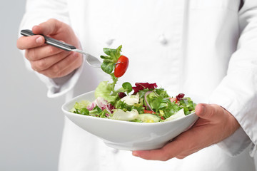 Handsome male chef with salad on light background, closeup