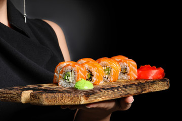 Beautiful woman with tasty sushi on dark background, closeup