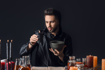 Male alchemist making potion on dark background