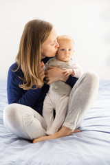 Fototapeta na wymiar Peaceful new mom hugging and kissing cute baby girl. Young woman nursing six month daughter in bedroom at home. Motherhood concept