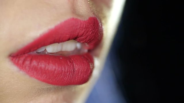 Detail close-up macro shot of the lips of a girl painted with a matte burgundy lipstick  blowing out the fire of a burning match on black studio background isolated. 4k slow motion 50 fps