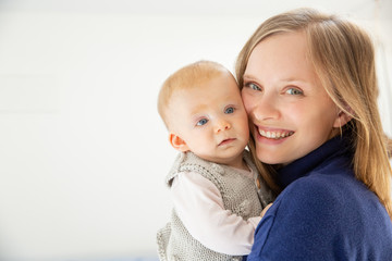 Happy mother and infant daughter smiling at camera. Portrait of happy young mother holding adorable infant baby girl isolated on white background. Parenthood concept
