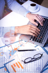 Businesswoman working on laptop with financial analysis graphs. Close-up of female hands typing on...