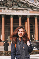 A brunette girl smiles against the background of the columns of St. Isaac's Cathedral in St. Petersburg