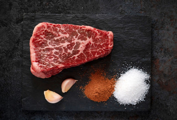 Raw flat iron steak from the neck of beef on a black background with salt and seasonings for the...