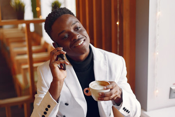 Black man in a cafe. Guy drinking a coffee. Man in a white jacket;