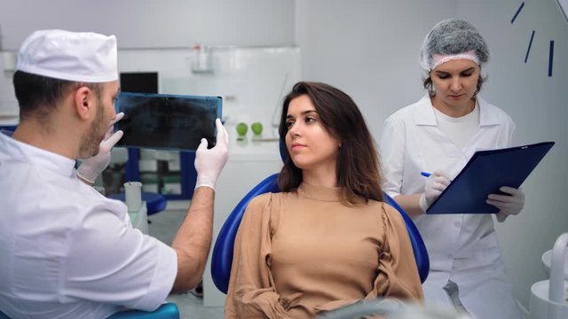 Male Dentist Analyzing X-ray Talking With Female Patient At Clinic. Medium Shot On RED Camera