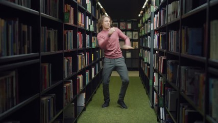 University Library: Handsome Caucasian Student Celebrates Successful Pass of Exams, Dances Between Rows of Bookshelves. Success in College: Admission, Graduations, Finishing Master Thesis