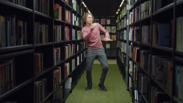 University Library: Handsome Caucasian Student Celebrates Successful Pass of Exams, Dances Between Rows of Bookshelves. Success in College: Admission, Graduations, Finishing Master Thesis