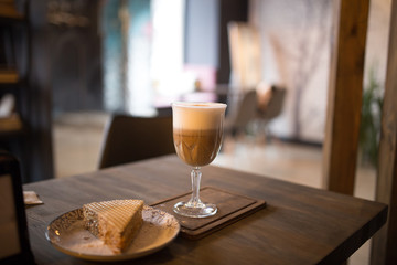 Cappuccino and a slice of cake on a table in a cafe.