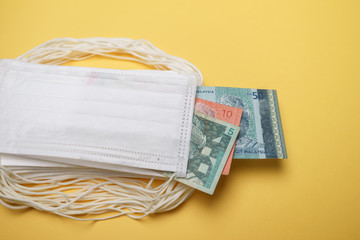 A pile of face mask with Malaysian money isolated over yellow background. Concept during Corona...