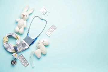 Stethoscope with cover, toys and pills on color background