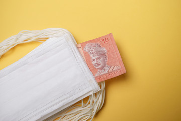 A pile of face mask with Malaysian money isolated over yellow background. Concept during Corona virus outbreak in Malaysia, shortage of face mask increase the demand in higher price.