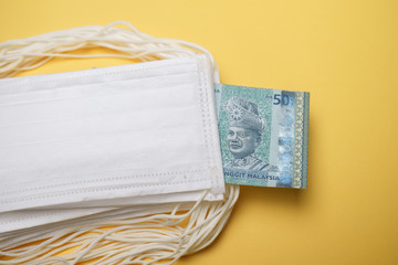 A pile of face mask with Malaysian money isolated over yellow background. Concept during Corona...
