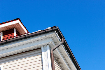 Exterior corner of a house with a roof, a rain gutter and a drainpipe for draining rainwater.
