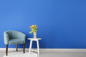 Interior of modern room with comfortable armchair and table with spring flowers near color wall