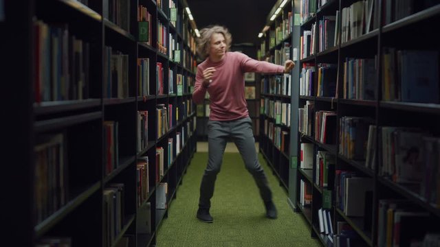 University Library: Handsome Caucasian Student Celebrates Successful Pass of Exams, Dances Between Rows of Bookshelves. Success in College: Admission, Graduations, Finishing Master Thesis
