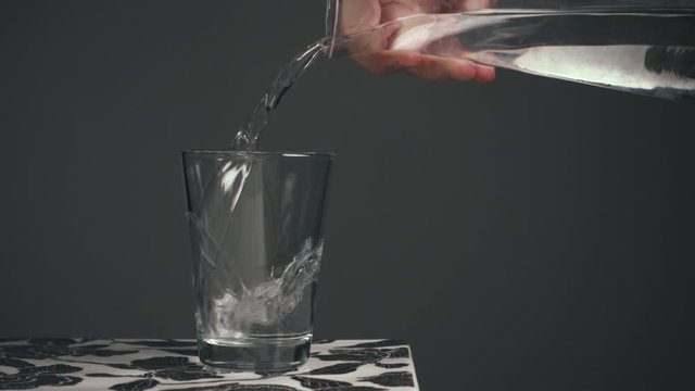 Dark moody backgroud, clean cinematic static shot, minimalistic, calm, clear empty glass, male hand pours water in the glass from a glass jug