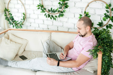 Naklejka premium Man using laptop and taking notes at home