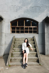 Fototapeta na wymiar Portrait of a beautiful, young and fashionable Thai Asian woman sitting on steps in the city