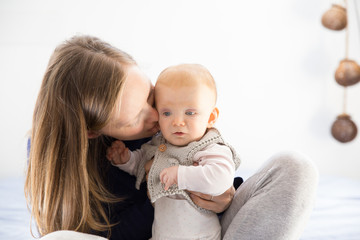 Happy playful new mom cuddling adorable little baby girl. Young woman nursing six month daughter in bedroom at home. Motherhood concept
