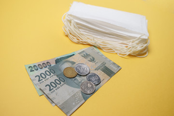 A pile of face mask with Indonesian Rupiah money isolated over yellow background. Concept during...