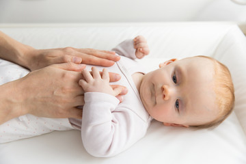 Parent touching tummy of adorable red-haired baby looking aside. Thoughtful newborn child relaxing in cradle. Nursery, newborn kid and infancy concept