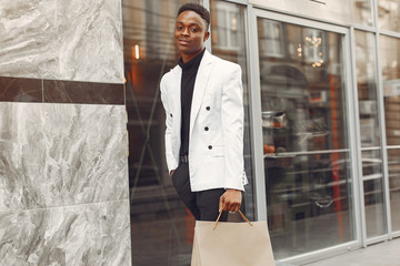 Black man in a city. Guy with shopping bags. Man in a white jacket.