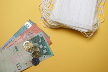 A pile of face mask with Malaysian coin and money isolated over yellow background. Concept during...