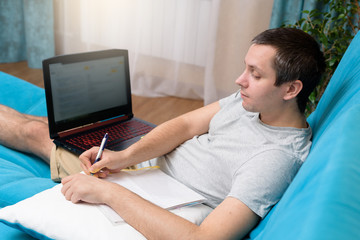 A man with a laptop on the sofa in the bedroom. Working from home during quarantine and self-isolation. Concept of quarantine, pandemic, coronavirus, online work, education, layout. Stay at home