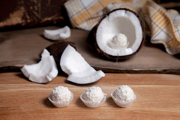 Coconut with white pulp and white candies on wooden background..