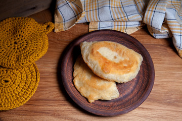 Clay plate of fried meat pies on wooden table.