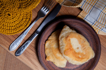 Clay plate of fried meat pies with cutlery on wooden table.