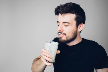 Young man isolated over background. Guy in black casual look hold glass of sour milk and enjoy drinking it. Side view of male person on picture. Thirsty.