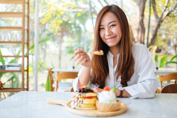 A beautiful asian woman eating a mixed berries pancakes with ice cream and whipped cream by wooden spoon