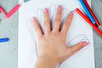 Girl draws with multi-colored felt-tip pens on white paper