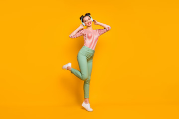 Fototapeta na wymiar Full length profile photo of pretty lady enjoy warm spring day traveling listen earphones wear casual red white shirt green pants sneakers isolated bright yellow color background