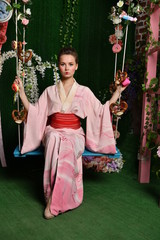 girl in japanese kimono posing on the background of flowering plants