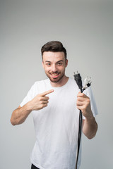 Young man isolated over background. Cheerful positive guy hold cord with socket in hand and point on it. Master ready to repair socket. Vertical picture of handsome positive master.