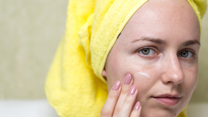 A girl with a towel on her head smears face with cosmetic cream, closeup. Natural cosmetic concept. Skin care, acne treatment, moisturizing skin.