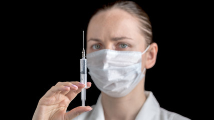 A syringe with a medicine injection in the hands of female doctor in white medical gown with sterile face mask on black background. Anti virus human health concept. Medicine and vaccination. 