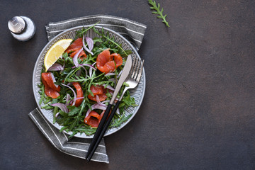 Salad with arugula and salmon on the kitchen dark table. Top view with place for text.