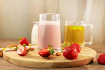 Fresh strawberry, almond and tea smoothie. With colored eco paper straws. On a wooden round board on a background of a concrete wall. Side view.