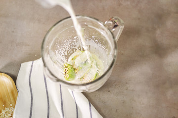 Skim milk is poured into a blender, which contains kiwi, oats and a banana. For a healthy and nutritious smoothie. Concrete background and white striped kitchen towel.